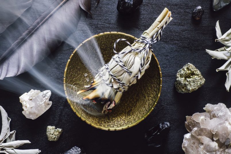 Samhain Smudging Rauhnächte, Räuchergefäß, Messingschale, Salbeibündel, Rauch, Kristalle, goldenes Erz, Obsidan, Vogelfeder, weiß, gold, ocker, grau, schwarz