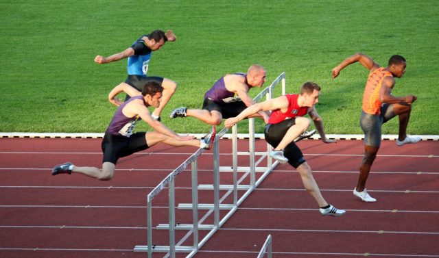Hürdenlauf Energetisches Feng Shui, Jahreskreisfest Lughnasad, Hürdenlauf, 5 Hürdenläufer in verschieden stadien des Sprungs, Hürden, Tartarnbahn, Rasen, grün,rot, weiß schwarz, lila, blau, orange
