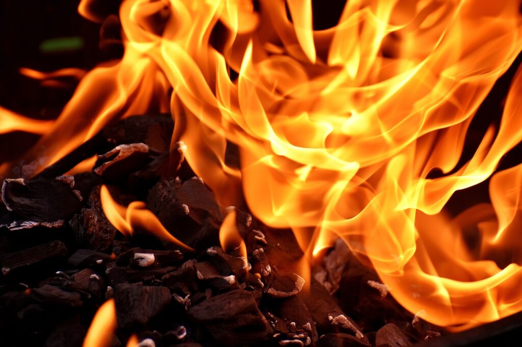 Energetisches Feng Shui, Elementarkraft Feuer, glühende Holzkohle mit lodernden Flammen, schwarz, lila, weiß, orange, gelb