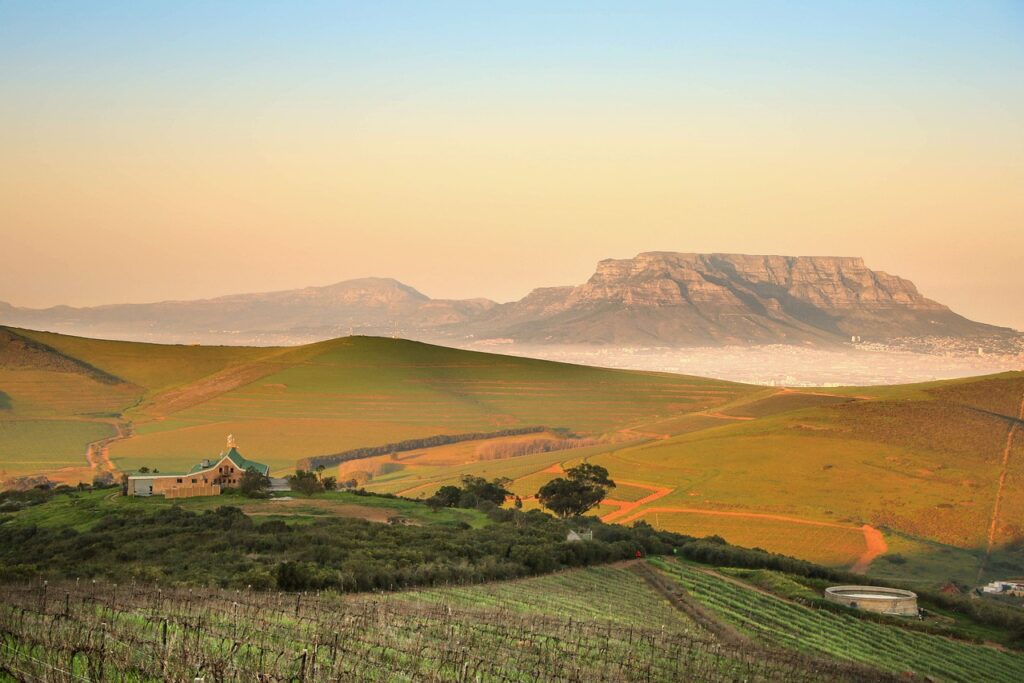 Energetisches Feng Shui, Elementarkraft Erde, hügelige Landschaft mit Feldern und Farm mit Tafelbergen im Hintergrund, ocker, grün, altrosa